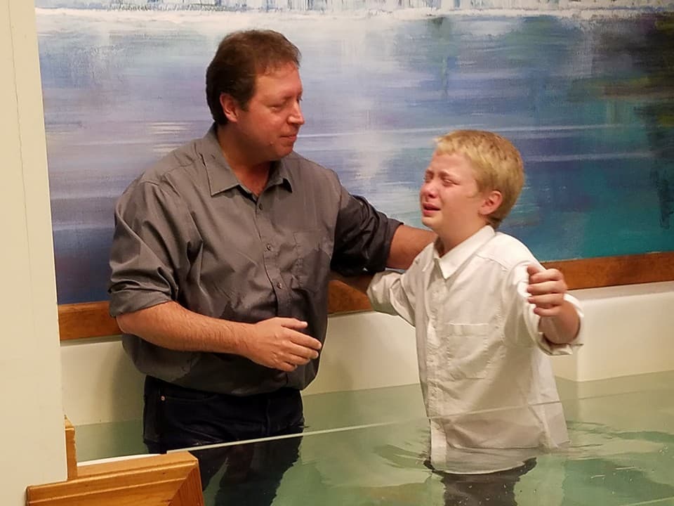 Pastor Benson praying over a young boy at the front of the sanctuary before his baptism.