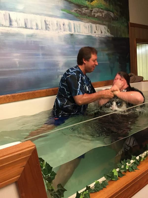Pastor Benson baptizing a woman by immersion in the LOTC baptistry, in front of a painted waterfall mural.