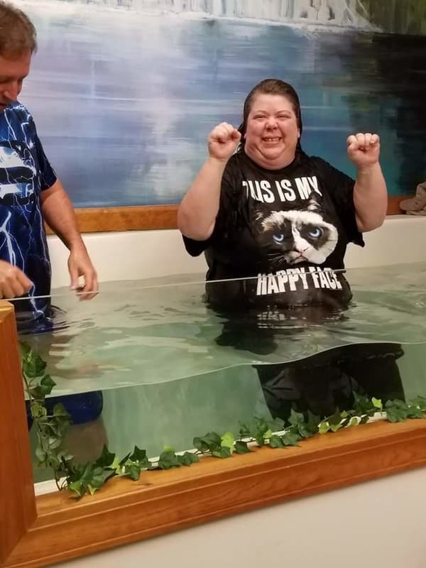 A woman raises both fists in celebration in the baptistry after being baptized.