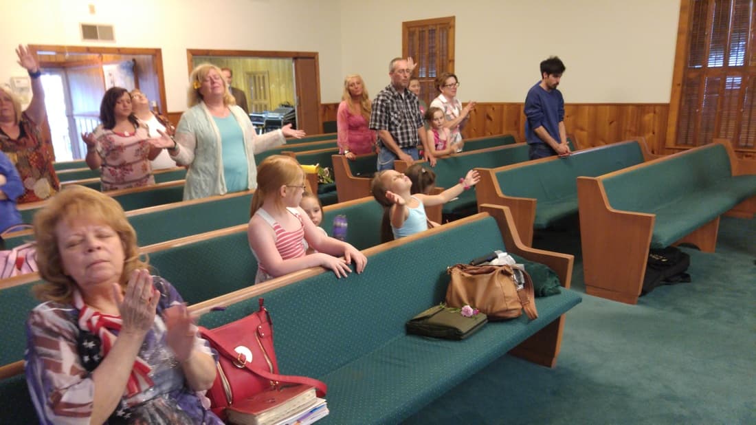 Members of the congregation standing and clapping in the teal pews during worship.