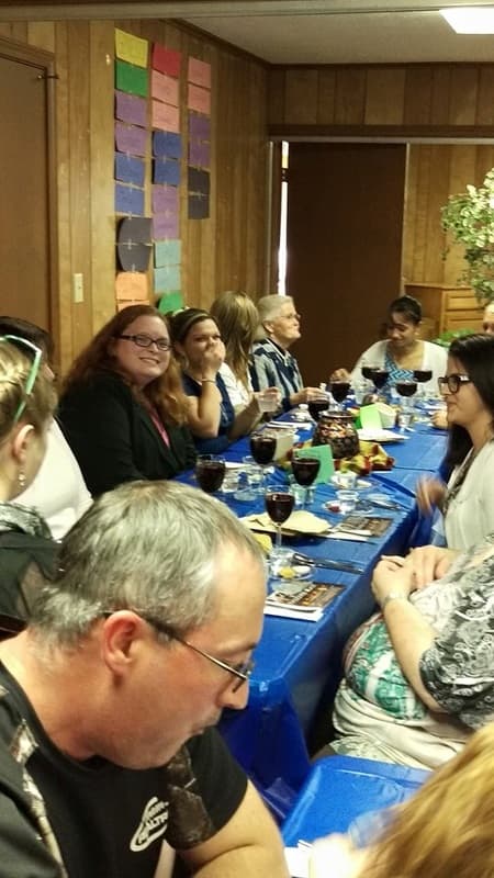 Church members seated along a long table sharing a fellowship meal.