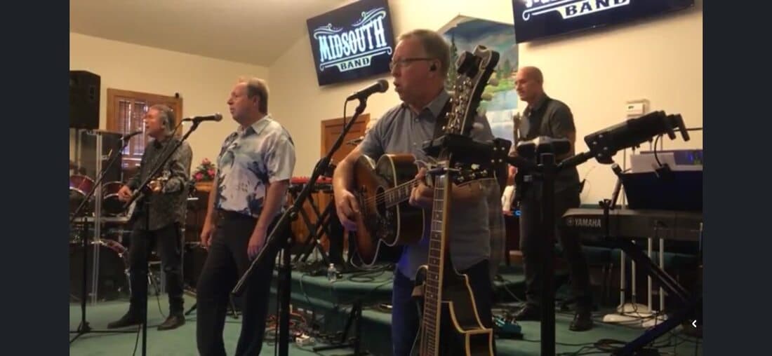 Pastor Benson singing with the Midsouth Band, guitars and microphones set up on the platform.
