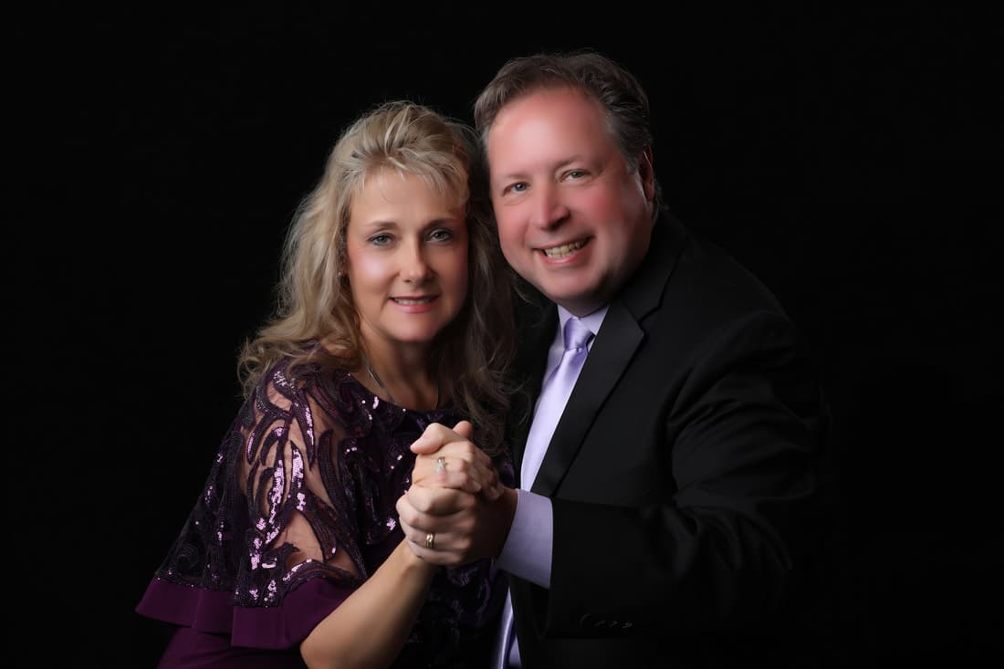 Pastors Joel and Beth Benson, photographed together against a dark studio backdrop.